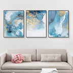 Three abstract art pieces in blue and gold on a wall above a sofa.
