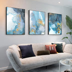 Three abstract art pieces on a wall above a sofa with decorative pillows.
