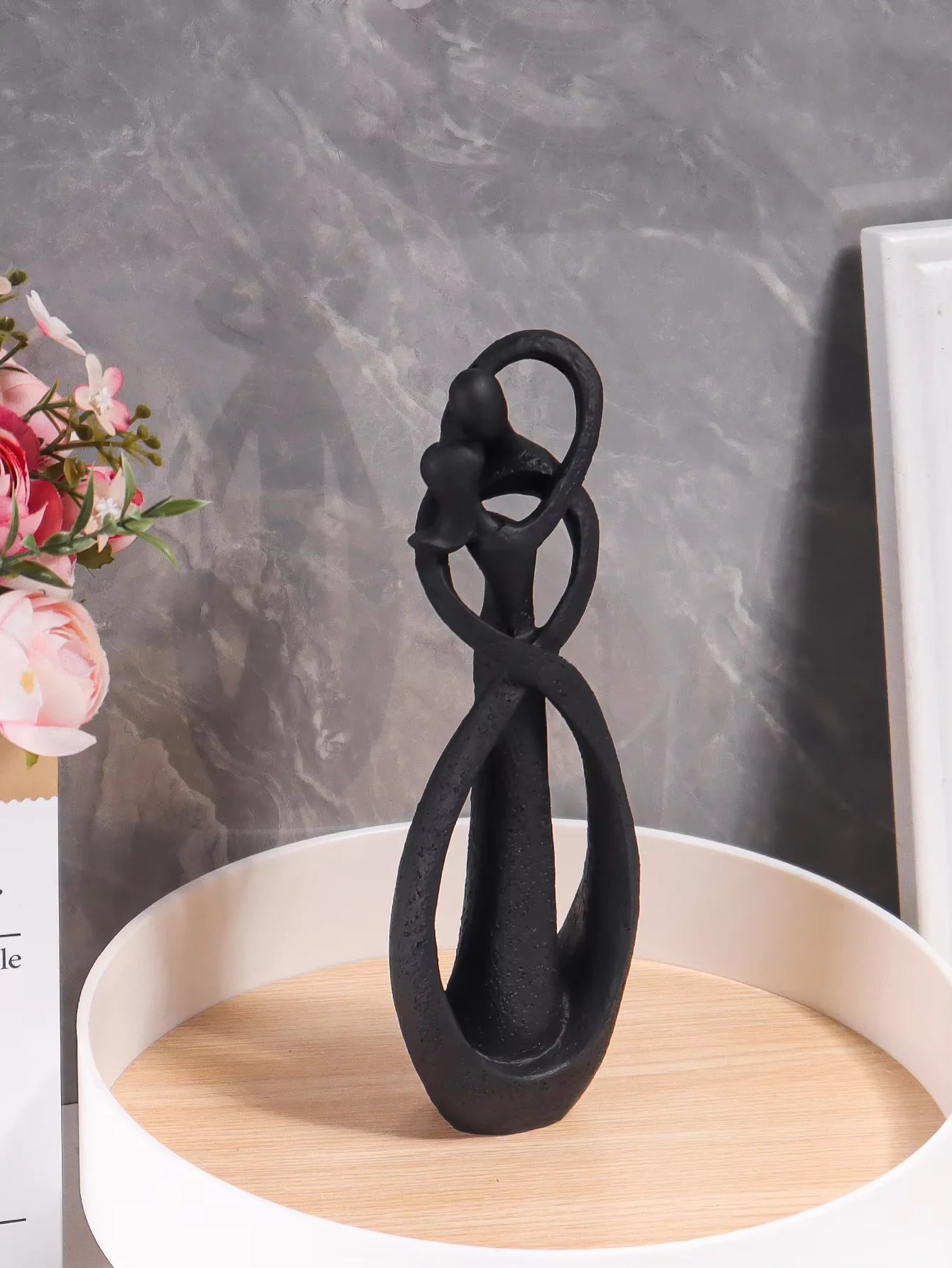 Black decorative object on a wooden stand with a marble wall background