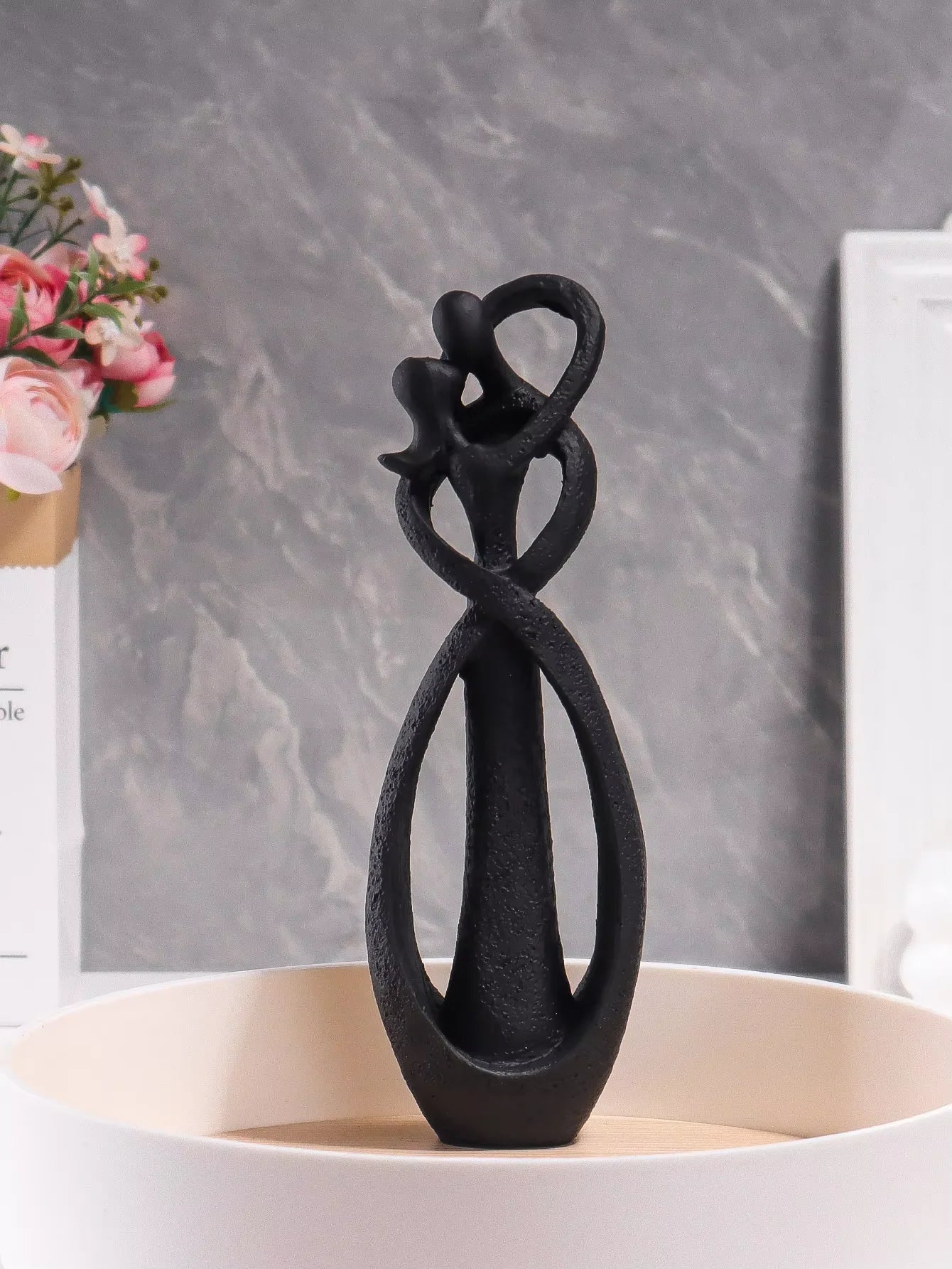 Black abstract sculpture on a white surface with a gray marble background