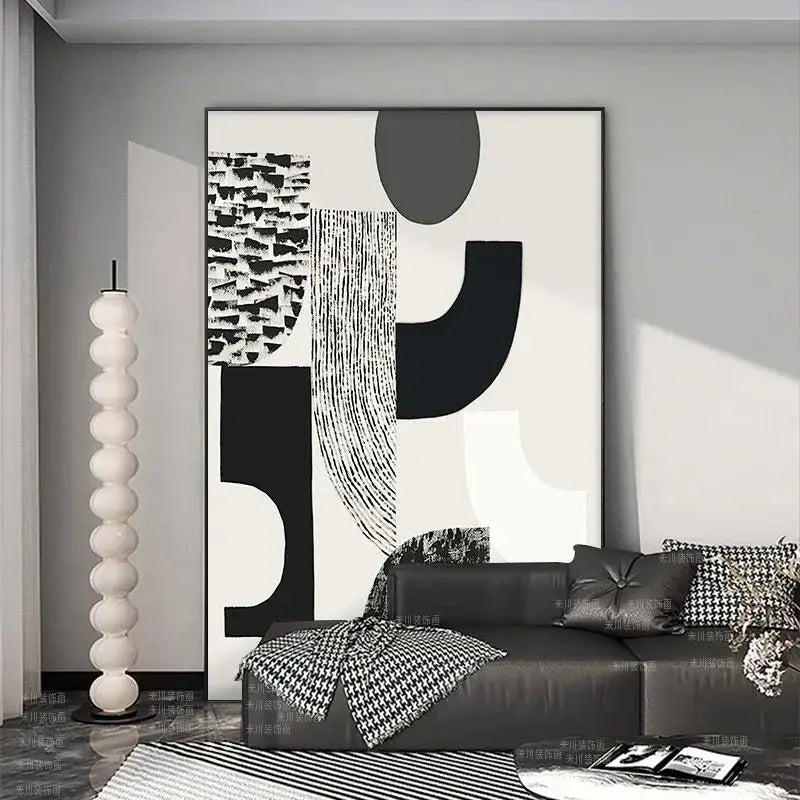 Modern living room with abstract black and white artwork on the wall, a black sofa, and decorative pillows.