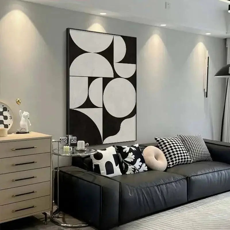 Modern living room with a black leather sofa, abstract wall art, and decorative items.