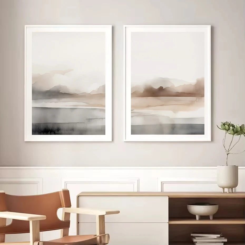 Two abstract art pieces in white frames on a wall with a chair and shelf in the foreground.