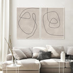 Two abstract line art prints on a wall above a sofa in a living room.