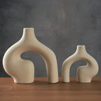 Two beige ceramic vases with organic shapes on a wooden surface against a dark background