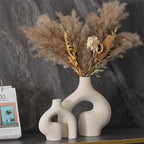 White ceramic vases with dried pampas grass arrangement on a dark surface.