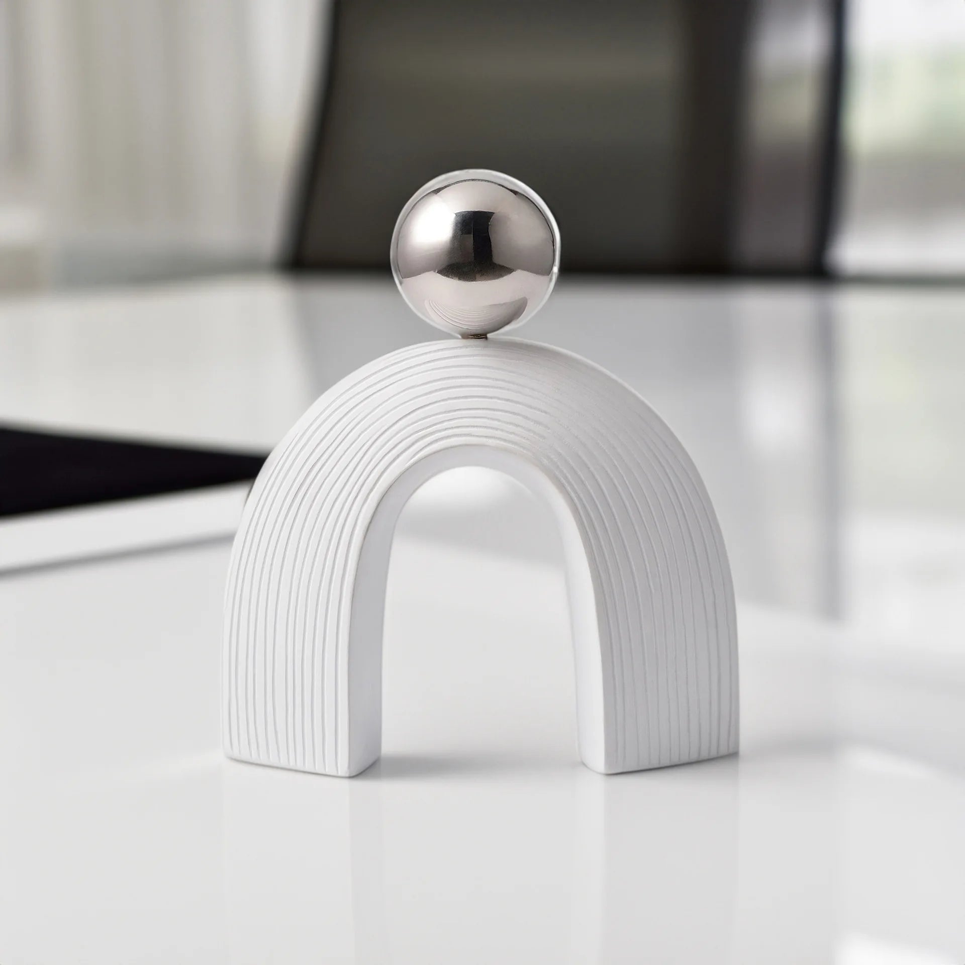 Decorative object with a white arch and silver sphere on a reflective surface