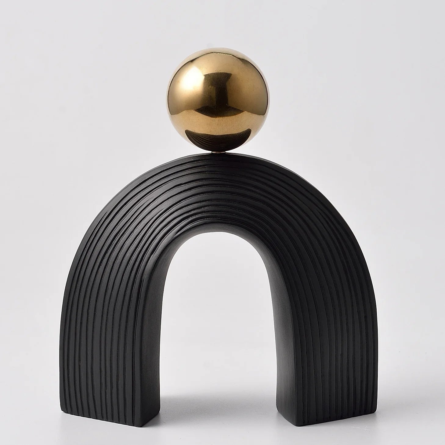 Black arch-shaped sculpture with a gold sphere on top against a light gray background