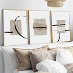 Three abstract art prints on a wall above a sofa with pillows.