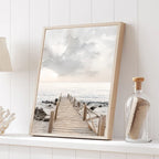 Framed artwork of a wooden dock leading to the ocean on a white shelf.