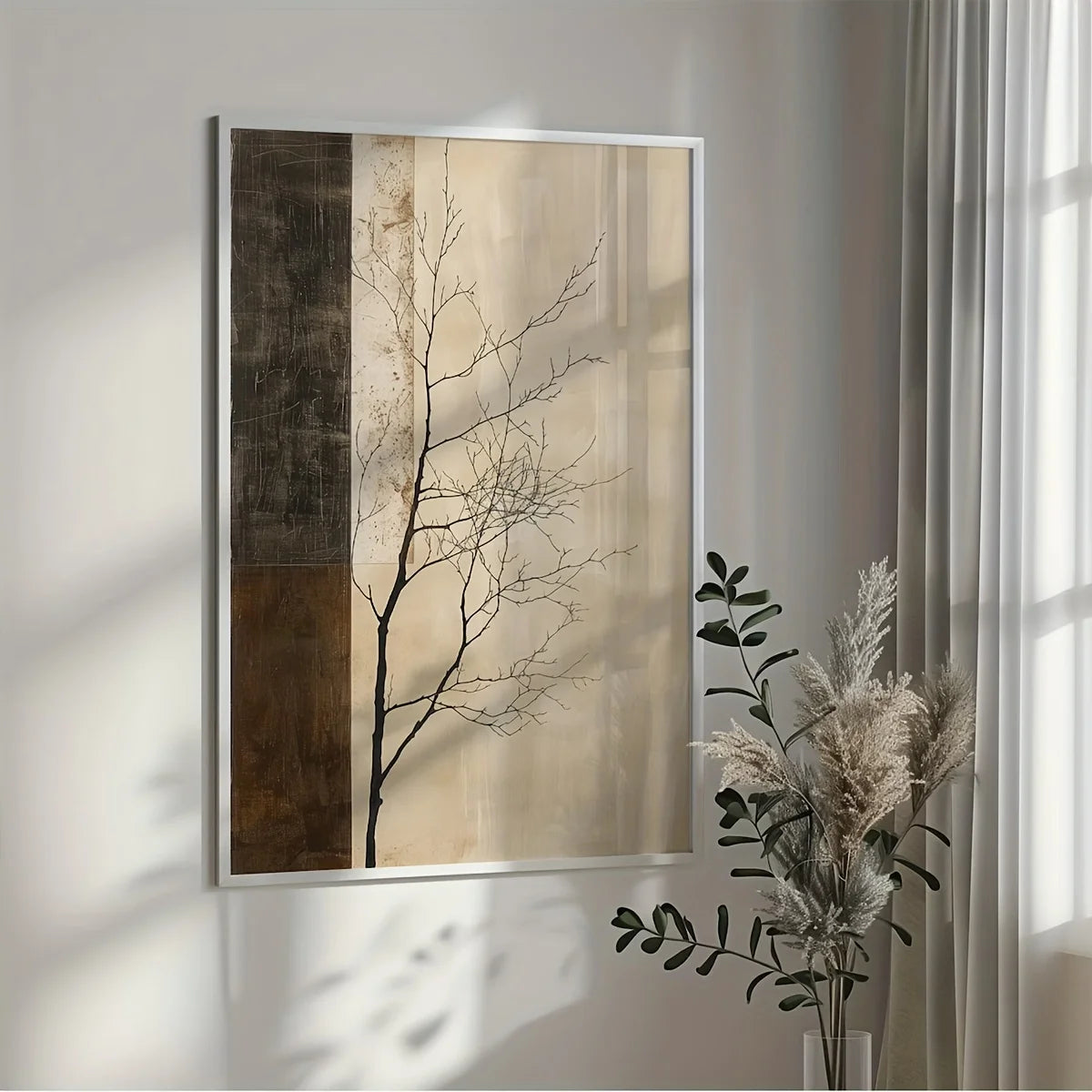A vertical framed wall art print with a minimalist tree design, hanging on a light gray wall in a styled room next to a vase of dried greenery.