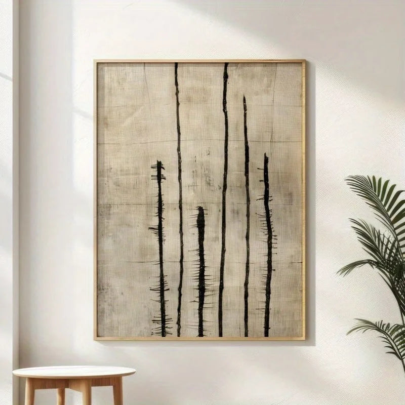 Minimalist abstract wall art hanging on a white wall, featuring vertical black brushstroke-like lines on a textured beige background, with a light wood frame. A small round table is partially visible at lower left and a green plant leaf is visible at lower right.