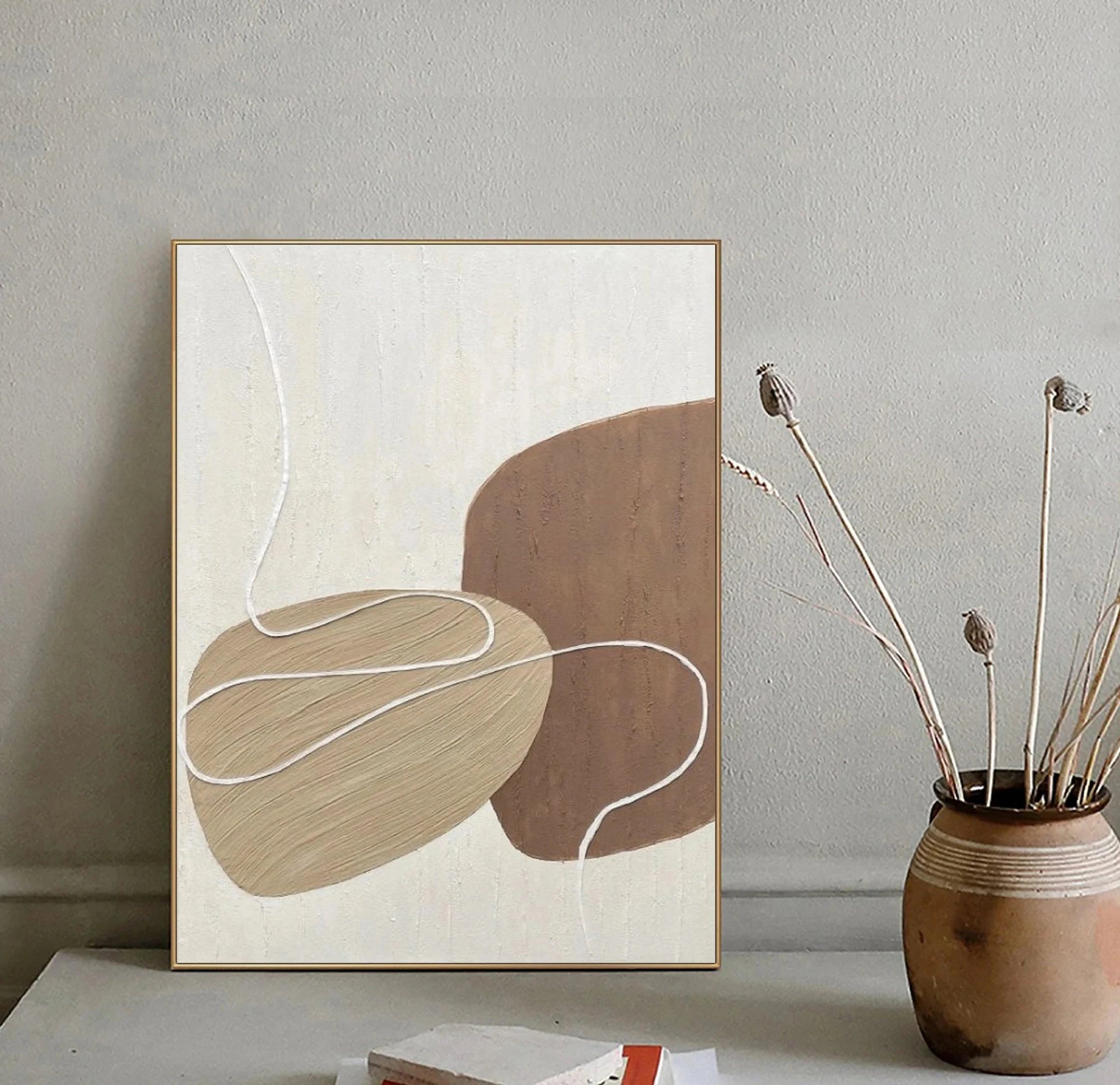 Abstract art print on a wall with a vase containing dried plants below.