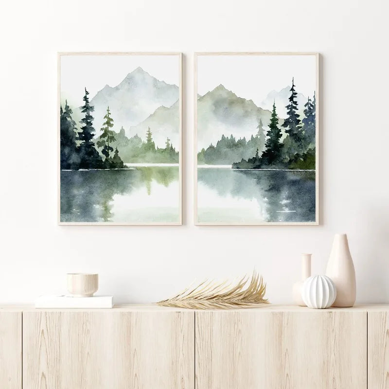 Two framed landscape paintings of mountains and trees over a lake on a white wall above a wooden shelf.