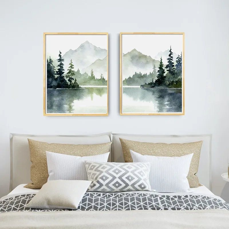 Two framed landscape paintings of mountains and trees above a bed with decorative pillows.