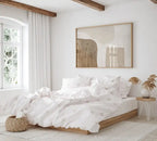 Neatly made bed in a bright bedroom with a large abstract painting on the wall.