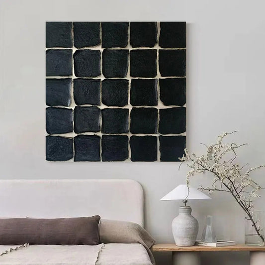 Black square wall art piece on a light gray wall above a sofa.