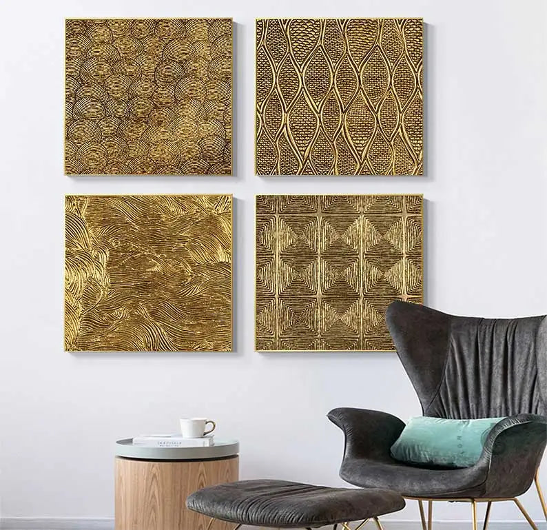 Four gold textured wall art pieces on a white wall with a modern chair and table in the foreground.