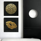 Two gold abstract art pieces on a wall next to a black cabinet with a white light fixture.