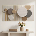 Abstract wall art with overlapping circles and vertical stripes in beige, taupe, gray, white, and gold tones, displayed above a console table with books, a vase of flowers, and a small decorative object.
