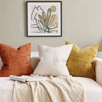 Decorative pillows on a sofa with a framed abstract art piece on the wall.
