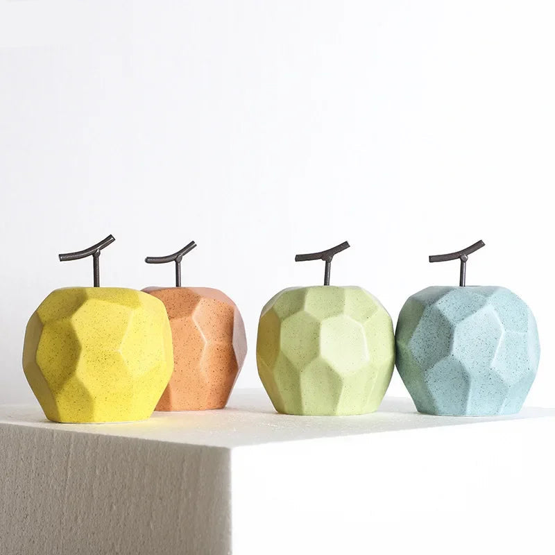 Four geometrically shaped apples in yellow, brown, green, and blue on a white surface.