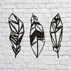 Three geometric feather-shaped wall decorations on a white brick wall.