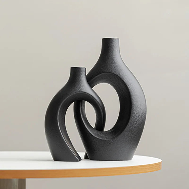 Two black abstract vases on a white surface with a neutral background