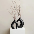Two black ceramic vases with circular designs on a white pedestal against a beige background