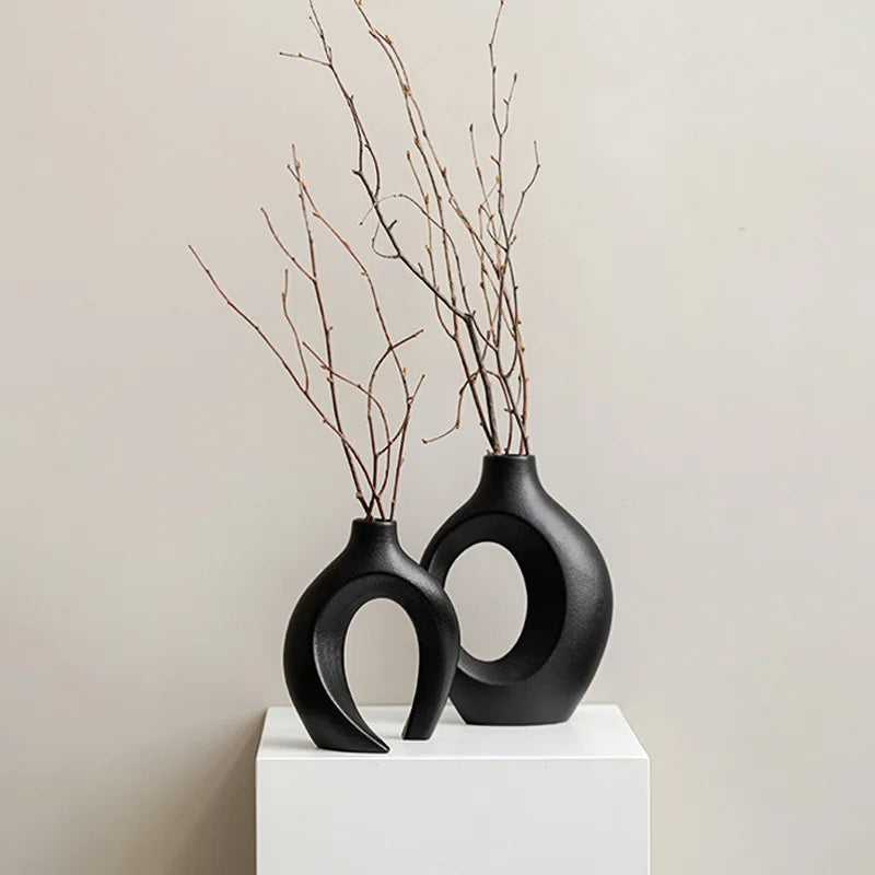 Two black ceramic vases with circular designs on a white pedestal against a beige background