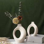 Two white ceramic vases with circular designs, one holding flowers on a dark green background.