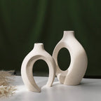 Two white ceramic vases with circular designs on a dark green background