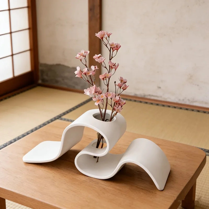 Modern white vase with pink flowers on a wooden table in a traditional room.