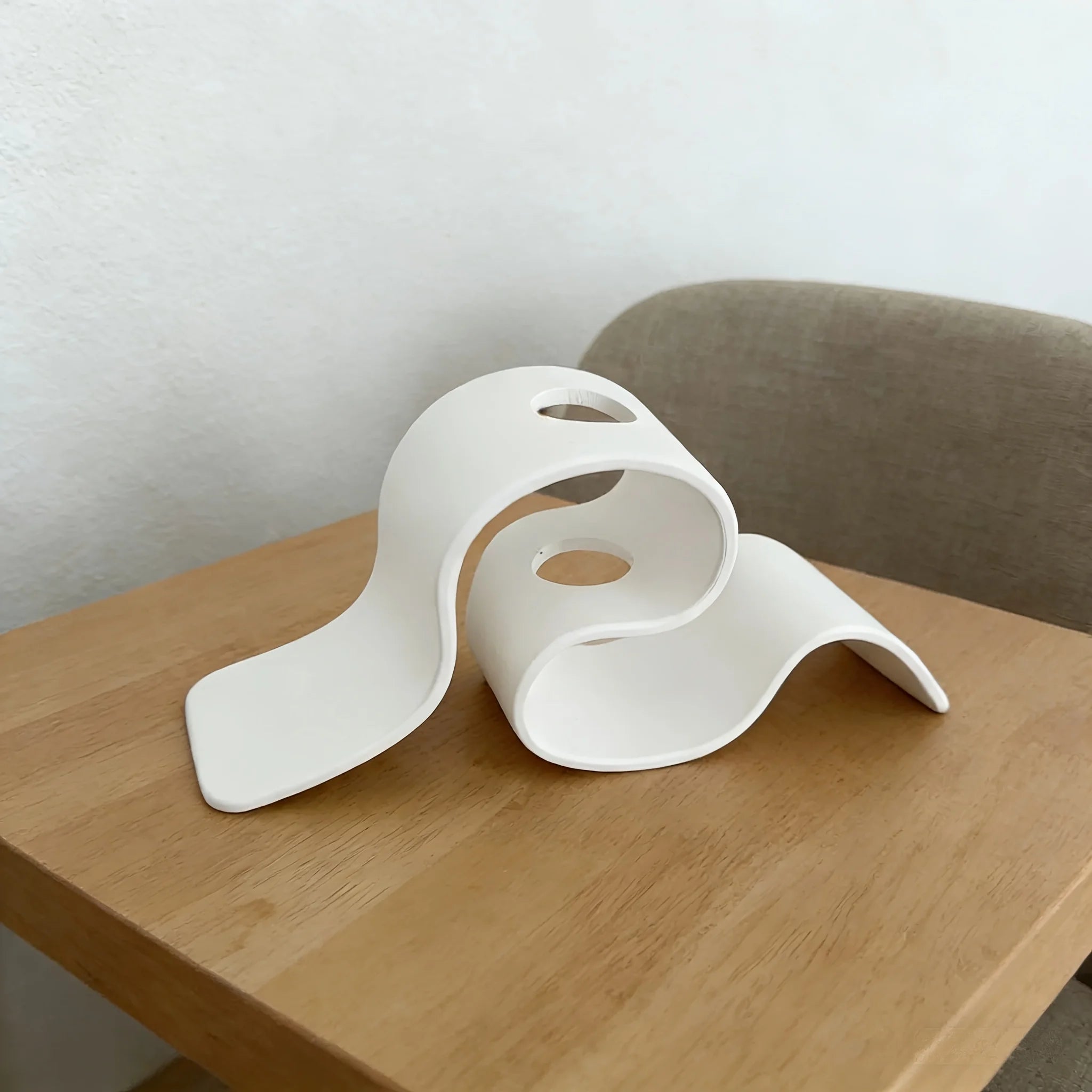 White abstract sculpture on a wooden table with a neutral background