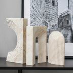 Three marble sculptures on a table with a black and white photo of a stone wall in the background.