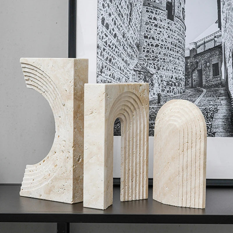 Three marble sculptures on a table with a black and white photo of a stone wall in the background.