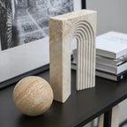 Decorative stone sphere and rectangular block on a dark surface with books and a framed picture in the background.