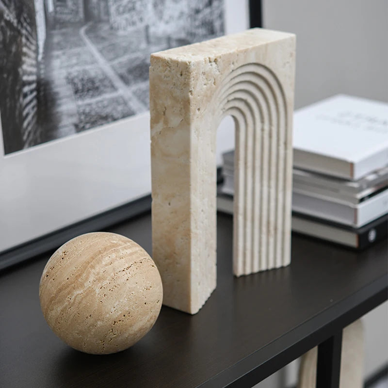 Decorative stone sphere and rectangular block on a dark surface with books and a framed picture in the background.