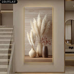 A wall art print displayed in a modern interior hallway. The artwork shows three beige and brown ceramic vases filled with tall cream pampas grass and small dried red stems, set against a light wood plank background with a thin gold frame.