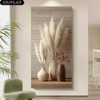 A vertical wall art print showing three beige and brown vases with pampas grass and dried flowers, displayed on a wall in a modern interior with a green chair and plant nearby.