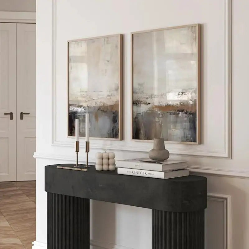 Two abstract paintings above a black fireplace mantle with decorative items.