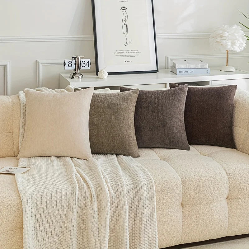 Beige sofa with patterned cushions and a blanket, with a side table in the background.