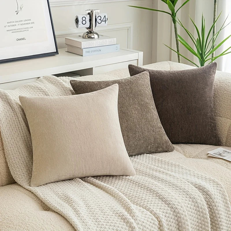 Beige and brown pillows on a sofa with a decorative plant and books in the background.