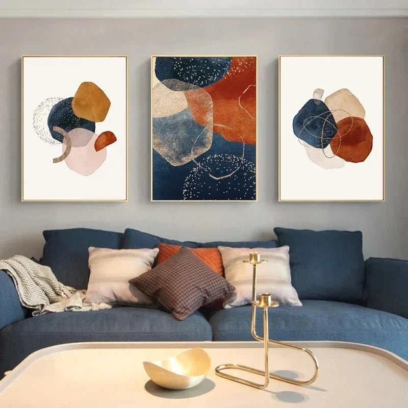 Abstract art prints on a wall above a blue sofa with decorative pillows.