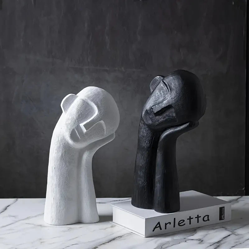 Two abstract sculptures, one white and one black, on a marble surface with a dark background.