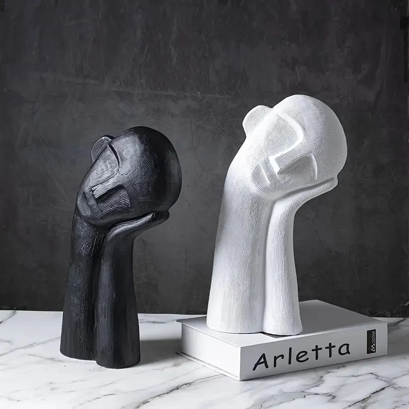 Two abstract sculptures, one black and one white, on a marble surface with a dark background.