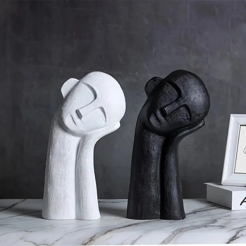 Two abstract sculptures, one white and one black, on a marble surface with a dark gray background.