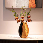 Gold vase with pomegranate branches on a white surface, framed artwork in the background