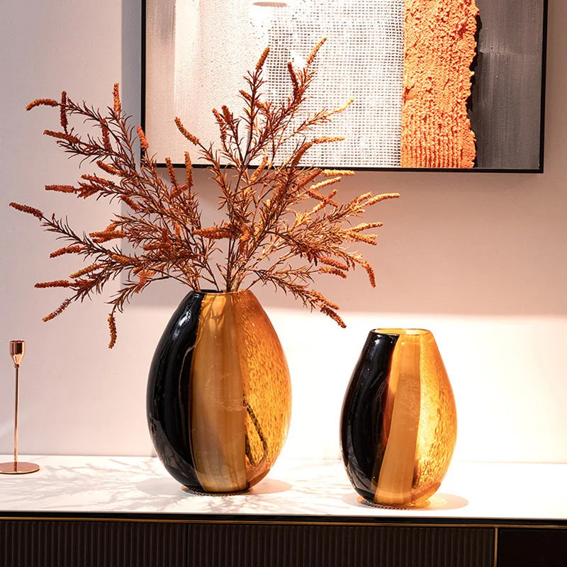 Two decorative vases with a black and gold finish on a surface, with a abstract painting in the background.