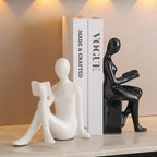 Two ceramic figures, one white and one black, holding books on a surface with a 'Vogue' book in the background.